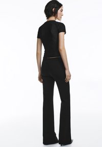 Crna uska majica kratkih rukava, uparen s crnim hlačama širokih nogavica. Glatki materijal, jednostavan dizajn i blagi sjaj.