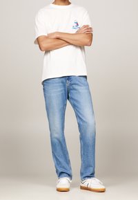 White cotton t-shirt with colorful printed logo on chest, paired with blue denim jeans and white sneakers with gum soles.
