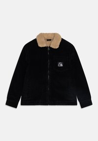 Chaqueta de pana negra con un collarete de piel sintética beige, cierre frontal con cremallera, bolsillo en el pecho y parche de logo en el lado izquierdo.