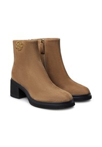 Stivaletti alla caviglia in suede color sabbia con finitura liscia, chiusura con zip, tacco basso a blocco e un sottile emblema decorativo dorato sul lato.