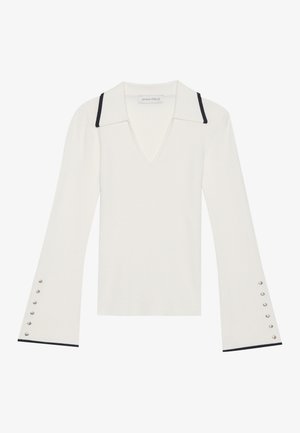 Pull en maille blanche à col en V avec un col pointu, doté de garnitures noires sur le col et de manches cloche avec des accents de boutons en argent.