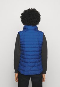 Chaleco acolchado azul con un alto cuello, diseño acolchado y corte sin mangas. La tela parece brillante, con una superficie lisa y texturizada.