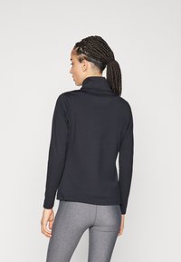 Top negro de manga larga con cuello alto, hecho de un tejido suave. La parte trasera presenta un diseño simple, combinado con leggings ajustados grises.