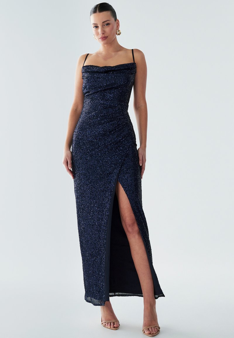 Navy sequin evening gown with a fitted design, cowl neckline, and side slit. Features thin shoulder straps and a straight hem.