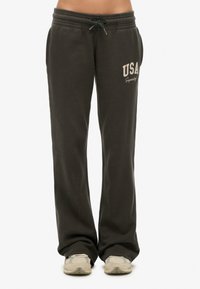 Grijze joggingbroek met een elastische tailleband en trekkoord. Heeft de tekst "USA" in beige op de linker dij. Zachte, gladde stof en losse pasvorm.