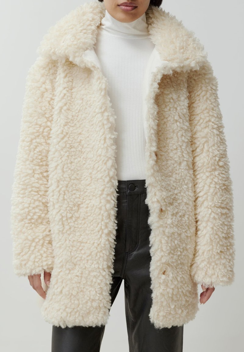Crème-kleurige faux fur jas met een gestructureerde, fluffy oppervlakte, grote kraag en knoopsluitingen, gecombineerd met een geribbelde witte coltrui.