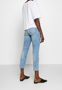 Bílá oversized tričko s krátkými rukávy, doplněné světle modrými slim fit džíny s vysokým pasem, roztrženými na kotnících. Černé slip-on boty.