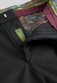 Schwarze Stoffhose mit glatter Textur, mit einem bordeauxroten Paisley-Futter, grünem Etikett und Reißverschlussdetail.