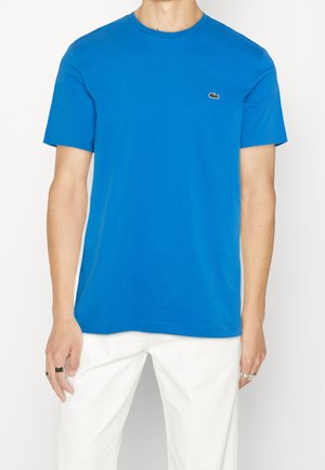 T-shirt en coton bleu à manches courtes, décolleté rond et petit logo vert sur la poitrine gauche. Texture lisse et coupe classique.