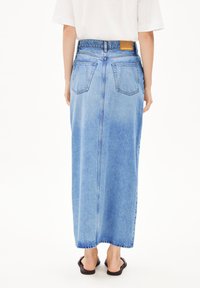 Lichtblauwe denim maxi rok met een rechte snit, voorzien van een tailleband, vijf zakken en een zichtbare naad in het midden van de achterkant.