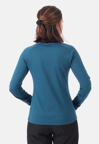 Turkusowa koszula z długim rękawem, z rękawami raglanowymi, slim fit, z płaskimi szwami i logo na górnej części pleców. Materiał wydaje się gładki i elastyczny.