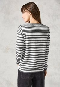 Gestreepte grijze en witte trui met een zachte textuur, lange mouwen en een ronde halslijn. Draagt bij donkere corduroy broek.