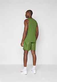 Top verde sem mangas combinado com calções verdes iguais. O tecido parece suave e leve, complementado por sapatilhas brancas e meias.