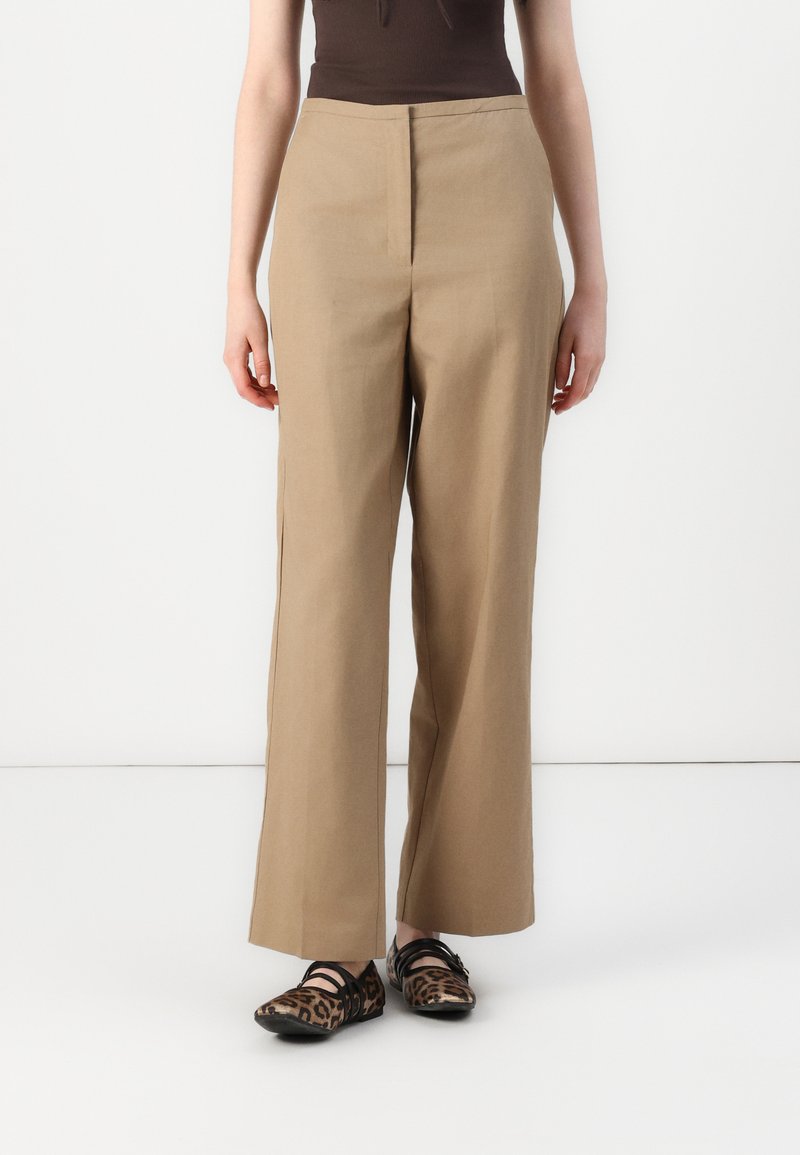 Pantaloni beige a gamba larga realizzati in tessuto leggero, con vita alta e linee pulite, abbinati a scarpe ballerine con stampa animale nera e marrone.