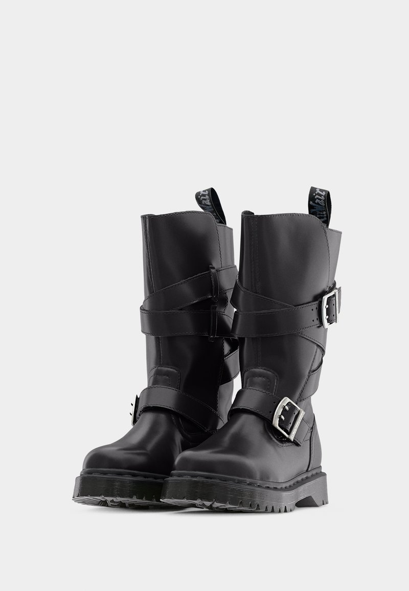Stivali neri in pelle fino a metà polpaccio con doppi cinturini con fibbia, suole spesse scanalate e linguette di sollevamento nella parte superiore su sfondo bianco.