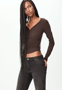 Haut en ribbed marron à manches longues avec un décolleté en V et des boutons noirs, associé à un jean gris foncé ajusté avec une poche avant et une légère décoloration.