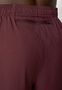 Bordo šorti ar elastīgu jostasvietu, gludu tekstūru un mazu rāvējslēdzēja kabatu aizmugurē drošai uzglabāšanai.