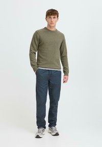 Olive green knit sweater, gray layered shirt underneath, paired with navy blue trousers and gray athletic sneakers. Simple, casual design.