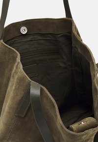 Sac fourre-tout en daim vert olive avec poignées en cuir foncé. L'intérieur comprend une étiquette et des emplacements pour cartes, mettant en valeur une doublure douce et texturée.