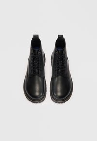 Par de botas de cuero negro con cordones hasta el tobillo, con acabado texturizado y suelas de goma gruesas sobre fondo blanco.