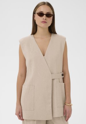 Bezs színű ujjatlan mellény texturált anyagból, mély V-nyakkivágással, két elülső zsebbel és oldalt gombos záródással.