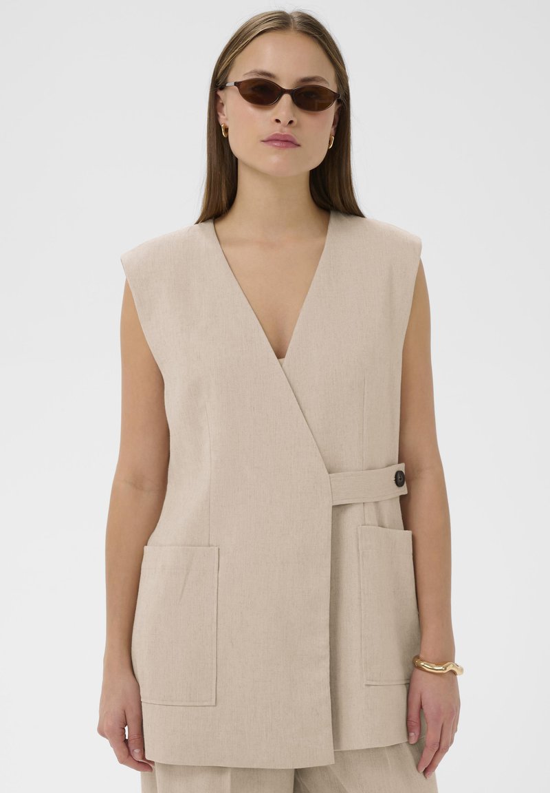 Beeživärviline varrukateta vest tekstuurse kangaga, sügava V-kaelusega, kahe eesmise tasku ja külgnööbli kinnitusega.