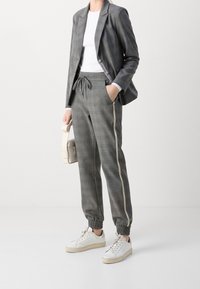 Grå rutmönstrad blazer med en figursydd design, kombinerad med matchande joggerbyxor med elastisk midja och sidopiping. Vita sneakers med låg profil.