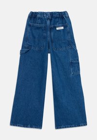 Denim hlače širokega kroja z elastičnim pasom, dvema sprednjima žepoma in stranskim žepom za tovor. Tkanina je temno modre barve z zbledelim videzom.