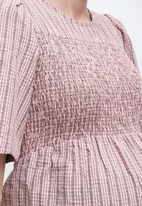 Κοντινό πλάνο ενός ατόμου που φοράει ροζ και καφέ ριγέ φόρεμα με ρυτιδωτό μπούστο και κοντά μανίκια.