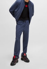 Laivaston bomber-takki, jossa on resorikaulus, musta logo-paita, räätälöidyt laivastonsiniset housut ja mustat lenkkarit, joissa on punaiset yksityiskohdat ja nauhat.