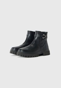 Bottes de cheville en cuir noir avec une finition texturée, semelle en caoutchouc épaisse et accent de boucle sur le côté. Présente un design à enfiler.