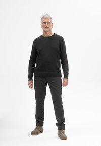 Zwarte gebreide trui, grijze broek en bruine veterschoenen. De trui heeft een ronde hals en ribgebreide manchetten; over het algemeen een gladde textuur.