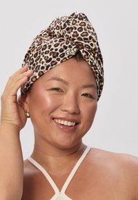 Foulard leopard stampato realizzato in tessuto, con un nodo legato nella parte superiore. Indossato da una persona con pelle chiara e un orecchino come accessorio.