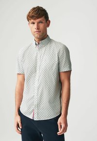 Camisa de botones de manga corta en gris claro con un patrón de diamantes, que presenta un bolsillo en el pecho y un acento de color en el dobladillo lateral.