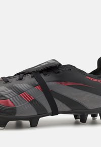 Black and gray soccer cleats with red accents, textured synthetic upper, lace closure, and multi-ground studs for traction.
