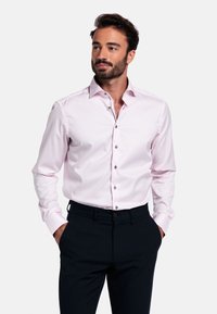 Lichtroze overhemd met een spread collar, zilveren knopen en lange mouwen, gecombineerd met donkere broeken. Gladde stofstructuur.