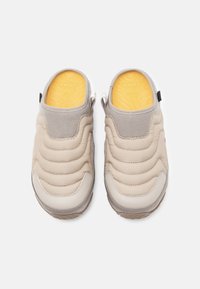 Beige slip-on klipklapper med en quiltet overdel og bløde grå accenter. Tekstureret gummisål med en gul indersål og en hæltræk-mønt for nem påtagning.