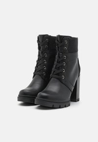 Bottines noires en similicuir avec un dessus texturé, bout rond et talon haut épais. Fermeture à lacets avec œillets métalliques.