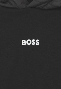 Černá mikina s kapucí s b�ílým logem "BOSS", které je výrazně zobrazeno ve středu. Text je tučný a jasný na tmavé tkanině.