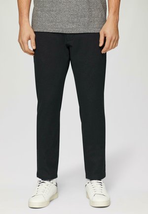 Schwarze Slim-Fit-Hosen aus Baumwolle, mit glatter Textur und minimalen Nahtdetails, kombiniert mit weißen Sneakern.