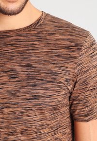 Braunes, strukturiertes T-Shirt mit einem dezenten gestreiften Muster, rundem Halsausschnitt und kurzen Ärmeln. Der Stoff wirkt weich und leicht.