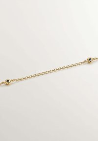 Pulsera de cadena de oro con acentos redondos de esmalte negro, con tamaños de eslabones alternos y un diseño delicado y texturizado.