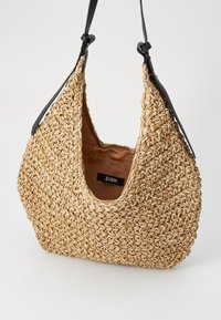 Wiklinowa torba z luźnym, hobo kształtem. Posiada czarny skórzany pasek oraz beżowe wnętrze z metką. Teksturowany zewnętrzny materiał w naturalnym kolorze.