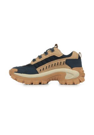 Zapatillas de deporte con una mezcla de ante y malla azul marino y marrón, con una suela de goma beige gruesa con profundas ranuras y líneas horizontales en el lateral.