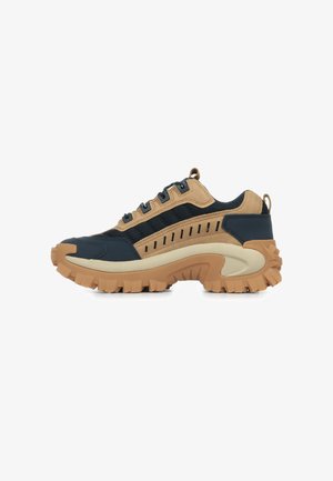 Sneakers con una combinazione di suede blu navy e tan e mesh, dotate di una suola in gomma beige spessa con scanalature profonde e linee orizzontali sui lati.