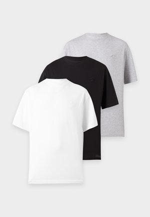 Dos personas de pie una al lado de la otra, vistiendo camisetas blancas de gran tamaño, pantalones sueltos de color gris claro y zapatillas negras contra un fondo blanco liso.