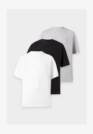 Deux personnes debout côte à côte portant des t-shirts blancs oversize, des pantalons amples gris clair et des baskets noires sur un fond blanc uni.