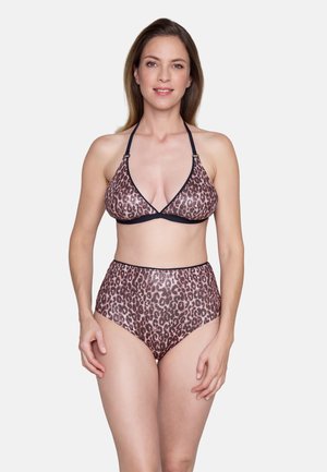 Vrouw staand en glimlachend in een tweedelig bikini met luipaardprint, bestaande uit een haltertop en hoog taille broekje, tegen een effen witte achtergrond.
