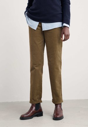 Brown corduroy pants with straight legs, rolled cuffs, paired with a navy sweater and a light blue striped shirt underneath. Brown ankle boots.