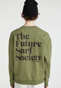Oliwkowy sweatshirt z okrągłym dekoltem, z dużym czarnym napisem "The Future Surf Society" na plecach, wykonany z miękkiego materiału.